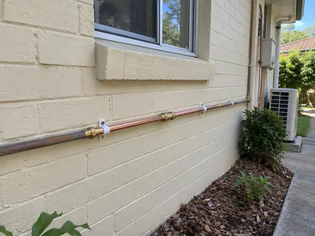 Repaired copper water pipe run on an exterior brick wall beside a window in Gymea Bay