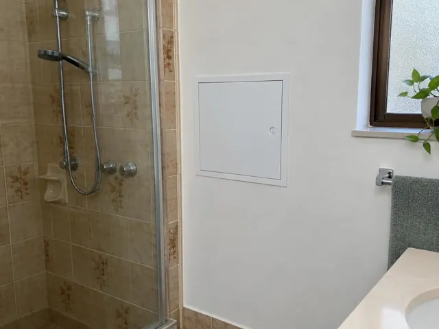 Bathroom wall with a neat access panel beside a tiled shower and window in Sutherland